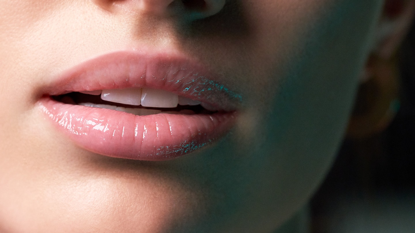 Close up moody photograph of a woman's mouth slightly open with glossy lips and a dark shadow on the right.